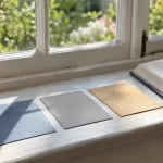 Tres tarjetas de colores junto a un libro con separadores sobre el alféizar.