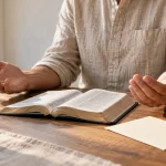 Persona con las manos abiertas junto a un libro y una tarjeta de lectura.